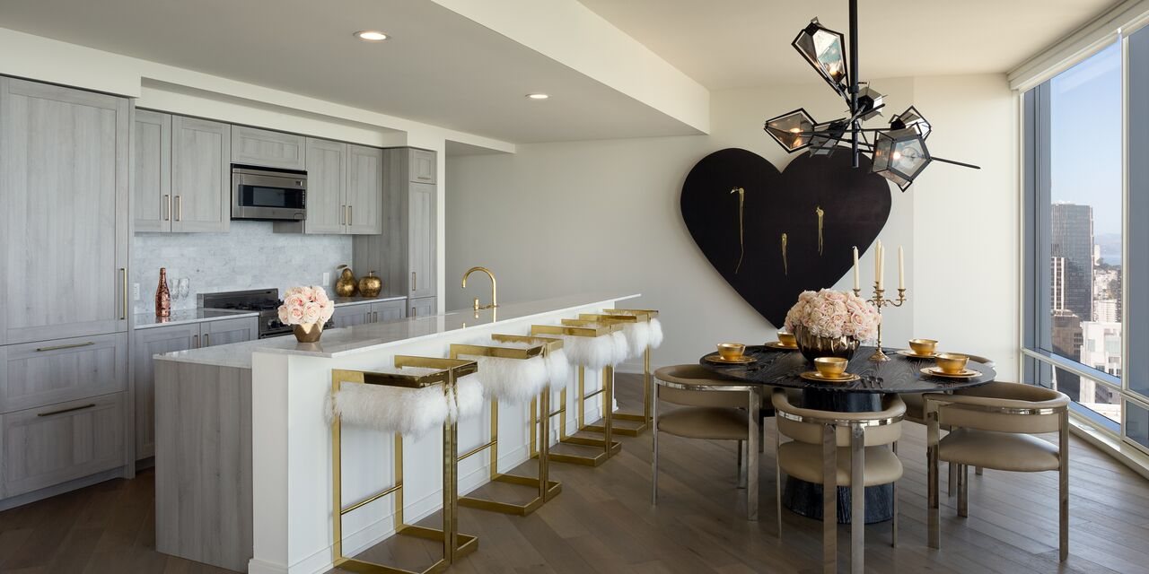 Large black heart with gold drips on a white wall beside a dining table with a view of the city