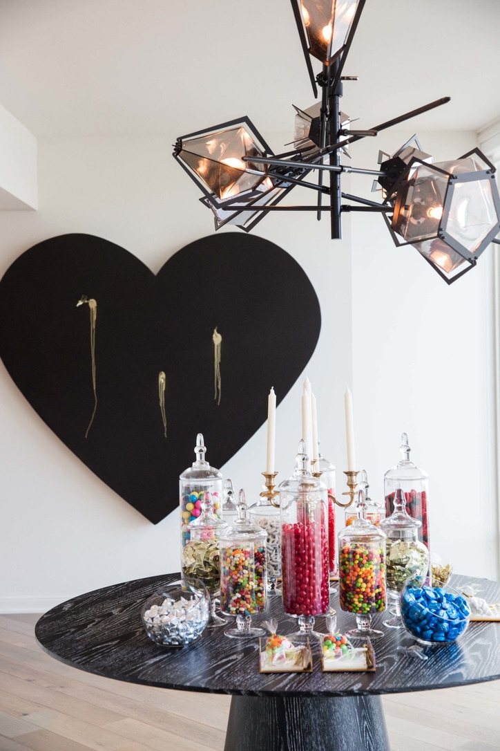 Black heart with gold arrows behind a table of candy jars under a sculptural chandelier