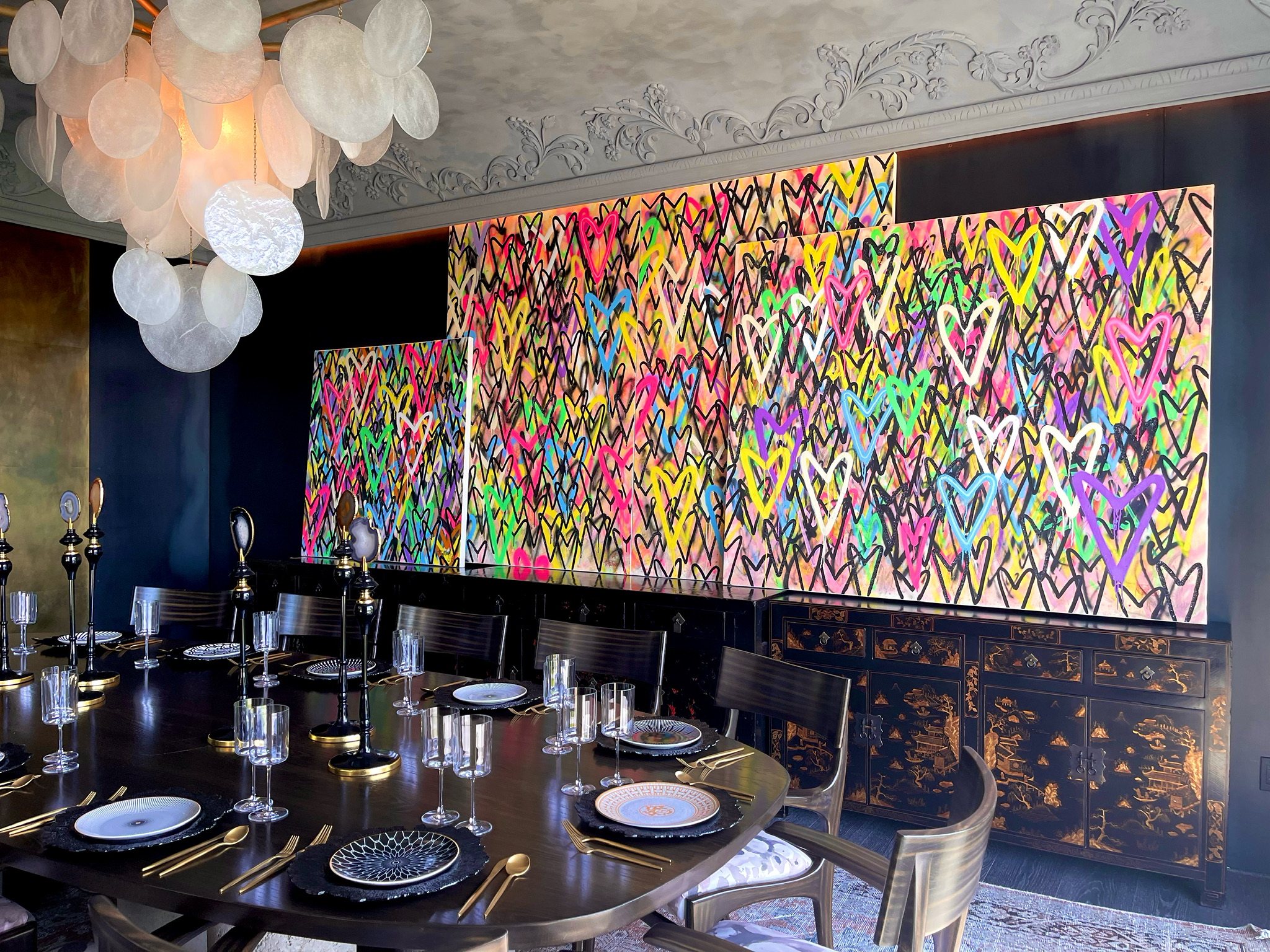 Three panels of multicolour spray-painted hearts above a lacquered sideboard in a dining room